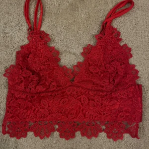 Röd/rosa spetsig linnetopp från Bik Bok - Säljer en röd/rosa linnetopp från Bik Bok med justerbara axelband och vacker spetsdetalj framtill och längs nederkanten. Toppen har en omlottkänsla och är fodrad med mjukt tyg på insidan. Perfekt för dig som gillar att sticka ut med färg och detaljer.