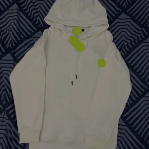 Vit hoodie med huva och ficka - Säljer en stilren vit hoodie i storlek S. Tröjan har en klassisk huva med snörning, ribbade muddar och en stor magficka framtill. Perfekt för dig som gillar enkel och clean streetstyle. Materialet är mjukt och skönt, skriv vid frågor om märke 