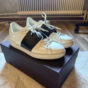 Valentino Garavani vita sneakers - Valentino Garavani Sneakers i Navy blue. Storlek 43. Skorna har använts vardagligen men med mycket försiktighet. Skorna är fortfarande väldigt vita, men har vissa små slitage här och där. Sätter därav skicket på 7,5/10.  All originalförpackning följer med, samt helt nya skosnören. 