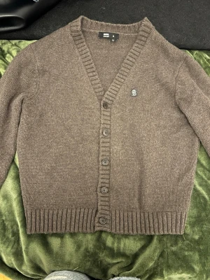 Brun stickad cardigan  - Mysig brun stickad cardigan från Dr. Denim med v-ringning och ribbade muddar. Perfekt att slänga på sig när det är kyligt ute.