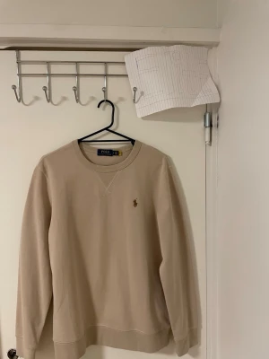 Beige sweatshirt från Polo Ralph Lauren - Snygg beige sweatshirt från Polo Ralph Lauren med klassisk rund hals och broderad logga på bröstet. Tröjan har lång ärm och är gjord i mjuk bomull som är skön mot huden. Perfekt för chill dagar och enkel att matcha med jeans eller joggers.Liknande modell som originala.