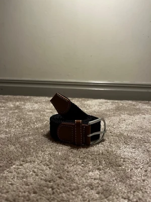 Flätat bälte från Ragazzo  - Ett stilrent flätat bälte från Ragazzo i en svart färg. Bältet är 105 cm långt och tillverkat i slitstarkt material som ger både komfort och hållbarhet. Den flätade designen gör bältet lätt att justera för optimal passform och passar lika bra till vardag som till mer uppklädda tillfällen.🍾🍾