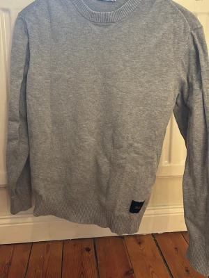 Grå sweatshirt från Tiger of Sweden/jeans - Säljer en enkel och stilren grå sweatshirt från Tiger of Sweden. Tröjan har rund hals, ribbade muddar vid ärmslut och nederkant samt en liten logotyp-patch nedtill. Perfekt för chill dagar och enkel att matcha med jeans eller joggers.