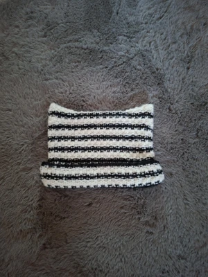 Randig stickad mössa i svart och vitt med kattöron   - Säljer en handstickad mössa  med horisontella svarta och vita ränder. Mössan har kattliknande öron och en grovstickad struktur som ger en cool och unik look. Perfekt att styla till en svart eller vit dunjacka för en trendig outfit.