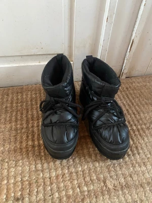 Svarta boots med snörning - Säljer ett par svarta boots. De har en puffig design, snörning framtill och grov sula för extra grepp. Skorna är tillverkade i syntetmaterial och har en rund tå. Perfekta för kalla dagar när du vill hålla dig varm och stilsäker.