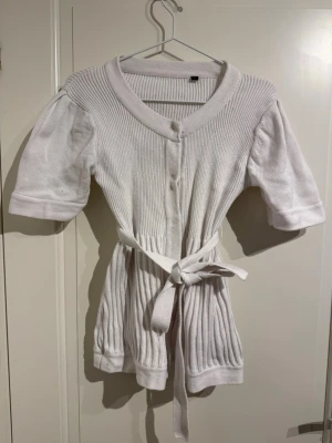 Stickad kofta med kort ärm  - Jättesöt kofta med knytband i midjan och tre knappar ovantill. 100% bomull.