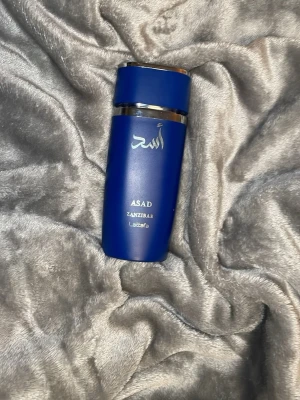 Asad Zanzibar av Lattafa - Snygg och modern parfym i blå  från Lattafa, Asad Zanzibar. Perfekt för dig som vill sticka ut med en unik stil. Volym och ingredienser framgår ej på bilden. Parfym är 100ml och har typ 70ml kvar 