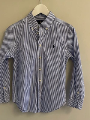 Blårandig skjorta från Ralph Lauren - Snygg skjorta från Ralph Lauren i blått och vitt med klassiskt randigt mönster. Säljer då jag har vuxit ur den. Den är i storlek 10-12 år. Hör av er vid funderingar. 