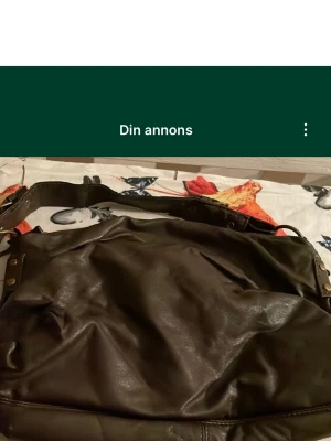 Mörkbrun axelväska i skinn - Säljer en mörkbrun axelväska från Åhléns i mjukt skinn. Väskan har bred axelrem med nitar och dragkedja upptill. Insidan har ett fack med dragkedja för småsaker. Perfekt storlek för att få plats med allt du behöver. Säljs på fler sidor.