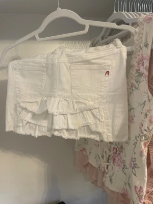 Vit jeanskjol från Replay - Vit kort jeanskjol från Replay med två bakfickor, volangdetaljer nedtill och ett litet rött Replay-märke på fickan.