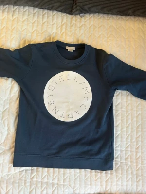 Mörkblå sweatshirt Stella McCartney - Snygg mörkblå sweatshirt från Stella McCartney med stort vitt cirkeltryck med loggan på mitten av tröjan. Strl 14 år men passar xs!