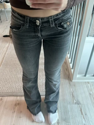 Bootcut jeans från Gina Tricot - Snygga mörkgrå bootcut jeans från Gina Tricot i storlek 158. Jeansen har låg midja, klassiska fem fickor och coola slitdetaljer vid bensluten. Materialet är jeans med en skön stretch och passformen är normal. Perfekta för dig som gillar en avslappnad stil.