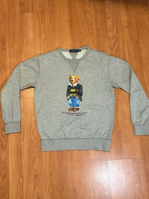 Grå sweatshirt Polo Bear Ralph Lauren - Säljer en grå sweatshirt från Polo Ralph Lauren i storlek S. Tröjan är knappast använd, max 2-3 eftersom den inte passade min stil. Tröjan har ett tryck med den ikoniska Polo Bear. Orginalpris ligger på 1700. 10/10 skick inga fel alls. Buda gärna!!