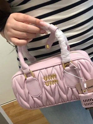 Ljusrosa quiltad handväska Miu Miu - Säljer en ljusrosa handväska från Miu Miu med quiltad design och guldfärgade detaljer. Väskan har ett snyggt mönster, dragkedja upptill och både handtag och axelrem. Perfekt för dig som gillar lyxiga accessoarer med unik look.