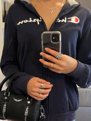 Champion hoodie - Snygg mörkblå hoodie från Champion med vit logga, dragkedja, huva och fickor framtill. Står storlek XL men passar XS-M.