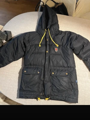 Fjällräven jacka - Den populära jackan från Fjällräven för en varm och skön vinter! Har några år på nacken men fortfarande mycket att ge!  Stor i storleken och passar allt från xs–m. Använd med vissa slitningar, se bild, därav priset. Inget som syns nämnvärt vid användning.  Dragkedja bytt men funkar fint. Saknar tre tryckknappar längst ner vid dragkedja, en lagning se bild. Smiter ut några dunfjun som det lätt kan bli med dunplagg främst vid vissa sömmar.  Pris är såklart ej fast pga skicket. Går ner till 1800kr 