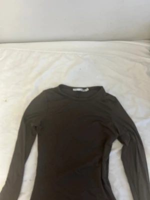 Brun långärmad topp från Lager 157 HELT NY!! - Slimmad brun långärmad topp från Lager 157 med rund halsringning. Materialet är mjukt och stretchigt, perfekt för lager-på-lager eller att bära som den är. Enkel och stilren design utan mönster eller detaljer, passar dig som gillar minimalistiskt.