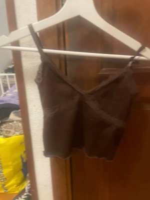 Brun ribbad linnetopp från H&M Divided - Säljer en brun ribbad linnetopp från H&M Divided i storlek XS. Toppen har tunna axelband, spetsdetaljer längs v-ringningen och är croppad i modellen. Perfekt för dig som gillar en enkel men ändå söt look.
