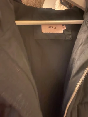 Svart pufferjacka från Nelly - Svart pufferjacka från Nelly med huva och grov dragkedja framtill. Jackan har quiltad design med breda kanaler och långärmade ärmar. Perfekt för kalla dagar och har en clean, stilren look som funkar till de flesta outfits.