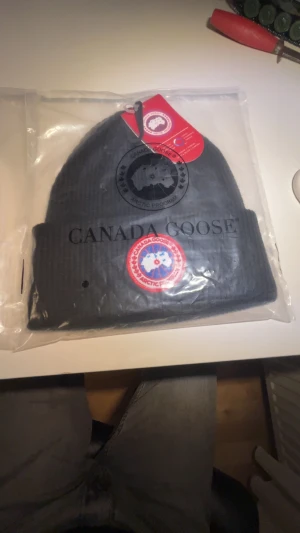 Svart ribbad mössa från Canada Goose - Pris kan diskuteras.Snygg svart mössa från Canada Goose med ribbad struktur och klassisk logopatch framtill i rött, blått och vitt. Märket är broderat. Mössan håller dig varm vilket är perfekt nu för vintern. 