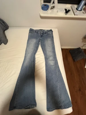 True Religion Joey Low Rise Flare Jeans - Säljer ett par ljusblå jeans från True Religion, modell Joey Low Rise Flare. De har låg midja och breda utsvängda ben, klassisk femficksdesign och snygga detaljer på bakfickorna. Perfekt för dig som gillar retrovibbar och statement-jeans.