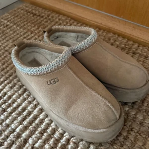 Beige UGG platform boots - Säljer ett par beige UGG boots med plattformssula och rund tå. Skorna är tillverkade i mjuk mocka med stickad detalj runt öppningen och har en fluffig insida för extra komfort. Perfekta för kalla dagar och har en stilren look.
