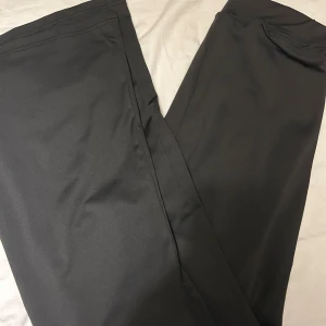 Svarta bootcut träningsbyxor  - Snygga svarta byxor med bootcut passform, perfekta för en chill och stilren look. Tillverkade i mjukt och följsamt polyestermaterial som ger en skön känsla. Byxorna har en enkel design utan synliga detaljer och passar dig som gillar minimalistisk stil.