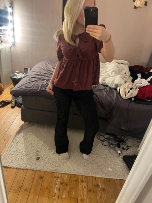 Mörk röd blus med rosetter  - Säljer en mörk röd blus från Lager 157 i storlek XS. Blusen har korta puffärmar, rosetter framtill vid halsen och ett flowy fall med rynkade detaljer. Materialet är lätt och har en snygg struktur som ger en fin look. Perfekt för dig som gillar en chill men ändå söt look. 🩷HELT NY🩷