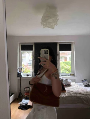 Brun quiltad axelväska från YSL - Säljer en brun quiltad axelväska från YSL med guldfärgad kedja och ikonisk YSL-logga framtill. Väskan har en mjuk, lyxig känsla i sammet och snygg omlottstängning. Perfekt storlek för det viktigaste och ger en classy vibe till din outfit.