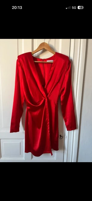 Röd omlottklänning i satin - Snygg röd kort omlottklänning från Reserved i glansigt satinmaterial. Klänningen har lång ärm, markerad midja med twist-detalj och djup v-ringning. Perfekt för dig som vill sticka ut med en färgstark look.