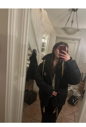 Svart dunjacka från Fjällräven XS - INTRESSEKOLL PÅ MIN JACKA. Svart dunjacka från Fjällräven med gul snörning och dragkedja framtill. Jackan har två stora fickor med knappar, hög krage och ett klassiskt Fjällräven-märke på bröstet. Perfekt för kalla dagar. Pris kan diskuteras