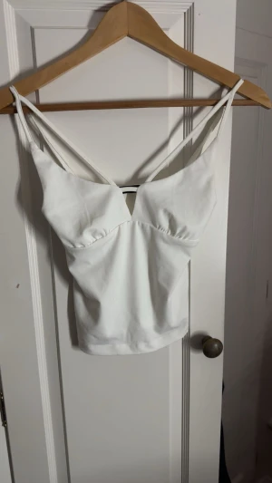 Vit croppad linnetopp från Bikbok - Säljer en vit croppad linnetopp från Bikbok i storlek XS. Toppen har smala axelband, v-ringad front och lätt rynkade detaljer vid bysten. Materialet är mjukt och har en lätt struktur, perfekt för sommarens alla tillfällen. Enkel och stilren design.