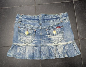 Blå jeanskjol med volang från Only - Säljer en kort jeanskjol från Only med cool tvättad look och volang nedtill. Kjolen har flera fickor, snygga gula knappar och kontrastsömmar i orange och grönt. Perfekt för dig som gillar streetstyle och denim. Märke syns på knapp och etikett.
