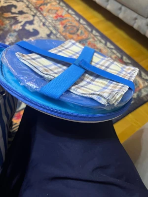 Picknickväska med bestick och tallrikar - Praktisk picknickväska i blått med randigt mönster, innehåller bestick, tallrikar och servetter för fyra personer. Allt är snyggt organiserat i fack och remmar. Väskan har axelrem och ser ut att vara i mycket gott skick, perfekt för utflykter och utomhusmåltider.