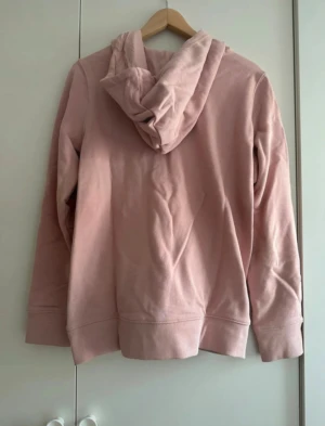 Rosa Adidas hoodie med logga - Säljer en rosa hoodie från Adidas med det klassiska trefoil-loggan i vitt framtill. Tröjan har huva med snörning och långa ärmar. Perfekt för både vardag och chill dagar