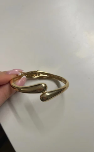 Guldigt öppet armband i metall - Snyggt armband i guldig metall med en öppen design och droppformade avslut. Perfekt för dig som gillar minimalistiska och moderna smycken. Armbandet är enkelt att ta på och passar till många olika stilar.