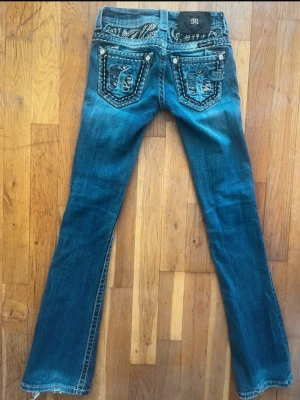Miss Me jeans w23 - Säljer ett par blå jeans från Miss Me med snygga zebra-mönstrade detaljer och strass på bakfickorna. Jeansen har kontrastsömmar, låg midja och bootcut-snitt 