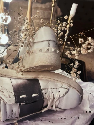 Valentino Garavani Rockstud sneakers - Säljer ett par Valentino Garavani Rockstud sneakers i vitt skinn med ett metallic-silvertryck över snörningen,  pyramidnitar runt hälen. Har används men vårdats väl. 