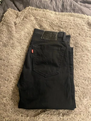 Svarta Levi's  jeans  - Snygga svarta Levi's jeans med klassisk femficksdesign och röd Levi's-tag på bakfickan. Jeansen har en slim passform och är tillverkade i mjukt jeansmaterial med stretch för extra komfort. Perfekt för dig som gillar en stilren och modern look.