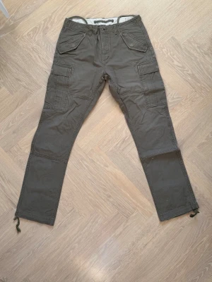 Olivgröna cargopants från Ralph Lauren - Säljer ett par olivgröna cargopants från Ralph Lauren med flera  fickor och snörning vid bensluten. Sparsamt använda. Nypris 3000