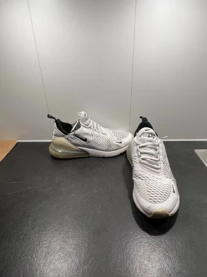 Nike skor  - Nike Air Max 270 sneakers i vit färg med svarta detaljer och synlig luftkudde i hälen. Ovandelen är tillverkad i ventilerande syntetmaterial med mesh och har snörning. Snygg och modern design med rund tå och platt sula, perfekt för dig som gillar streetstyle. Tveka inte på prisförslag.Dom är stretchiga och passar även för dom som har storlek 42  och 43. Använda ett par gånger men inget stort hål som ni ser på bilderna 