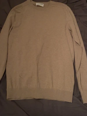 Beige stickad tröja från Selected Homme storlek S - Snygg beige stickad tröja från Selected Homme i storlek S. Tröjan har rund hals och långa ärmar, perfekt för lager-på-lager. Materialet är mjukt och skönt, och den neutrala färgen gör den enkel att matcha med olika outfits.