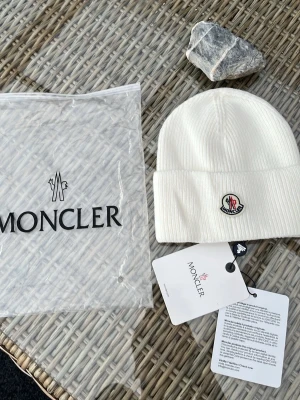 Vit Moncler mössa - Säljer en clean och stilren vit mössa från Moncler i ribbstickad ull. Klassisk Moncler-logga framtill och bred uppvikt kant. Mössan är enkel att matcha och kommer med originalpåse och tags. https://code.moncler.com/?QR=35225294UPUY