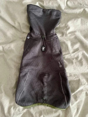 Mörkgrå fleeceväst från Hurtta - Säljer en mörkgrå fleecetröja från Hurtta med gröna detaljer och justerbar snörning. Västen har mjukt grönt innerfoder med hexagonmönster och öppningar för frambenen. Perfekt för kyliga dagar och passar mindre hundar. Hurtta Razzle-dazzle reversible midlayer hundjacka. Går att vända på och använda med fleecen inåt eller utåt.  Jätte fint skick, men tyvärr för stor för min vovve.  Storlek 30. Se bilder för mått.