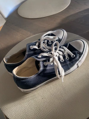 Converse All Star svarta sneakers - Svarta Converse All Star sneakers med vit tå och vit sula. Klassisk låg modell med rund tå, vita snören och tydliga kontrastsömmar. Ovandel i textil och yttersula i gummi. Perfekt för dig som gillar ikoniska och tidlösa sneakers.