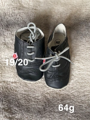 Svarta babyskor från Pax med snörning - Säljer ett par svarta babyskor från Pax med snygga grå snören och dekorativa sömmar. Skorna har rund tå samt platt sula. Perfekta för små fötter som vill se extra coola ut.🌸 Sparsamt använda . 19/20