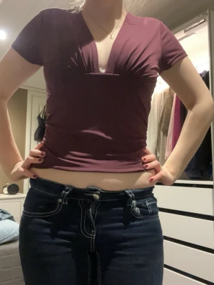 Vinröd v-ringad topp med rynk - Säljer en vinröd topp med v-ringning och snygga rynkdetaljer vid bysten. Toppen är kortärmad och har en figurnära passform som framhäver midjan. Materialet känns mjukt och stretchigt, perfekt för dig som gillar stilrena och enkla plagg med en twist.