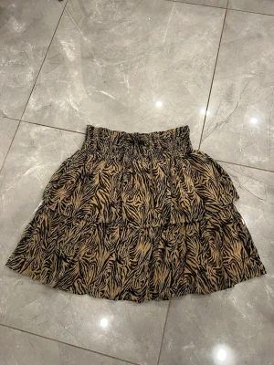 Zebramönstrad kortkjol från Y.A.S - Kjol från det eleganta skandinaviska märket Y.A.S i storlek L med zebramönster i svart och beige. Orginalpris är 800 kr. Kjolen har volanger och en smockad midja som ger en skön och flexibel passform. Materialet är lätt och luftigt, och kan passa någon som bär L eller M.