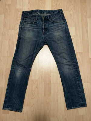 G-Star RAW blå jeans straight fit - Säljer ett par klassiska blå jeans från G-Star RAW med snygg slitning och raka ben. Jeansen har knäppning med knappar, fem fickor och detaljerad söm på bakfickorna. Perfekta för dig som gillar en tidlös och avslappnad look. Säljer dom då jag inte använder de längre. I byxorna står det EJ någon storlek, men jag använder ( vanligtvis ) 32/32 i mina jeans! Hör av er vid funderingar!✅
