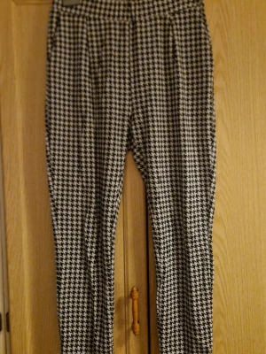 Svarta och vita rutiga byxor från Lager157  - Snygga ankellånga byxor från Lager157 i storlek M med hundtandsmönster. De har en elastisk midja och smalare ben, vilket ger en modern och chill look. Materialet känns mjukt och bekvämt. Kolla gärna in mina andra annonser! 